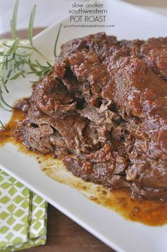 a white plate topped with meat covered in sauce and garnished with green herbs