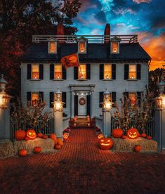 a large white house with pumpkins in the front yard and lights on at night