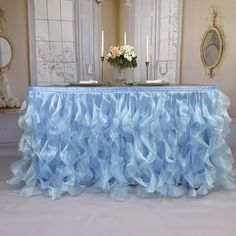 a table covered in blue ruffled cloth with candles and flowers on the table next to it