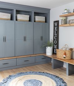 a living room with gray cabinets and blue rugs on the wooden floor, along with two shelves filled with wicker baskets