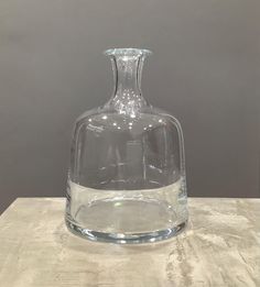 a clear glass vase sitting on top of a wooden table next to a gray wall