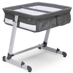 a grey baby crib with wheels and white sheets on the bottom, in front of a white background