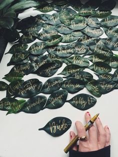 a woman's hand with a pen writing on some leaves that have names written on them