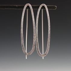 These earrings are curvy and sparkly with a decidedly modern edge - sure to please the art and design lover. The shimmering texture on the metal adds a little something unexpected, and is sure to draw lots of compliments. Featuring a narrow oval with subtle sparkle texture that catches the eye on the front, paired with a visible threader ear wire in the back, this design creates an intriguing and dimensional visual statement. 1.5" long with fixed wire threader ear wire. Available in sterling sil Modern Oval Earrings With Ear Wire, Modern Twist Silver Earrings For Everyday, Everyday Silver Earrings With A Modern Twist, Modern Oval Single Earring, Modern Sterling Silver Oblong Earrings, Modern Oblong Sterling Silver Earrings, Modern Handmade Oblong Earrings, Silver Oval Single Earring, Modern Oval Sterling Silver Hoop Earrings