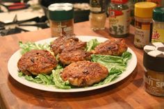 some meat patties are on a plate with lettuce and seasoning next to it