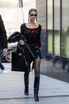 a woman walking down the street carrying a black bag and wearing high heeled boots