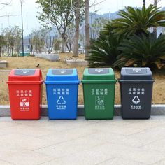 four different colored trash cans sitting next to each other on the sidewalk in front of some trees