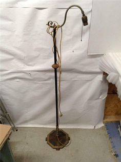 an old floor lamp is standing in front of a white sheeted wall and it's cord wrapped around the pole