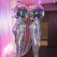 two women in shiny silver outfits standing next to each other with disco balls hanging from the ceiling