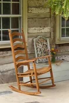 a wooden rocking chair sitting on top of a sidewalk next to a tree and window