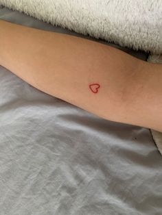 a person laying in bed with a red heart tattoo on their arm and the other arm