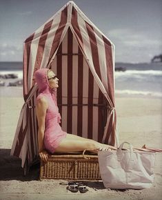 a woman in a pink bathing suit sitting on a beach next to a striped tent