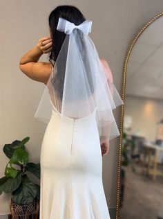 a woman wearing a white wedding dress with a veil on her head, looking at herself in the mirror