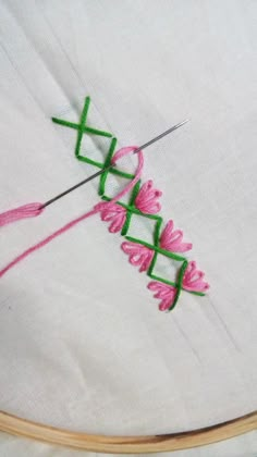 a close up of a pink flower on a white cloth with a green stitcher