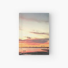 the sun is setting over water with boats in it hardcover book on a white background