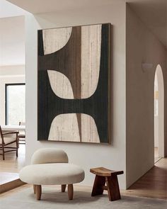 an abstract painting hangs on the wall above a white chair and footstool in a living room