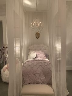 a bed with white curtains and a chandelier hanging from it's ceiling