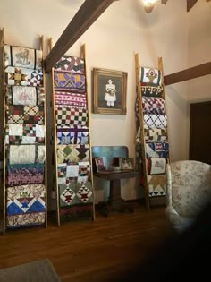 a room filled with lots of quilts next to a chair and wall mounted pictures