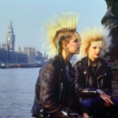 two women sitting next to each other in front of a body of water with buildings behind them