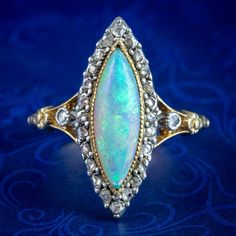 A striking antique opal navette cluster ring from the late 19th Century built around a mesmerising natural opal cabochon in the centre (approx. 2.5ct) that has been marquise-cut to match the gallery.  The opal displays a beautiful medley of colours that fade and intensify with the light and is framed by twinkling rose-cut diamonds around the border, with an additional diamond on each shoulder (approx. 0.28ct total).  Opal is the birthstone of October. Their magic has been revered throughout hist Luxury Victorian Gold Opal Ring, Floral Engraving, Edwardian Engagement Ring, Antique Jewelry Rings, Estate Rings, Gold Eagle, Diamond Settings, Memento Mori, Marquise Cut