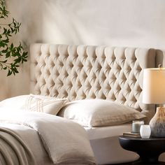 the headboard of a bed with white linens and pillows, next to a night stand