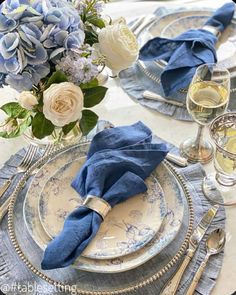 the table is set with blue and white plates, silverware, and flowers in vases