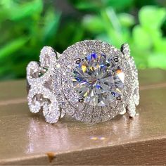 a diamond ring on top of a wooden table with green plants in the back ground