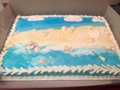 a blue and white birthday cake with seashells on the beach in a box