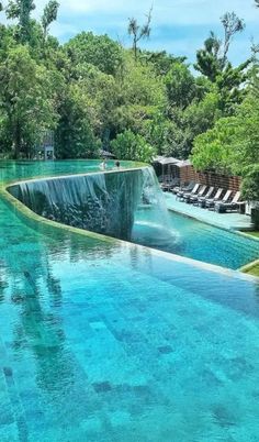 an outdoor swimming pool surrounded by lush green trees and water features a waterfall running down the side