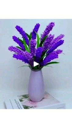 purple flowers in a white vase on top of a book