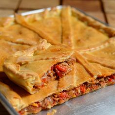 several slices of meat pie on a metal tray with a wooden table in the background