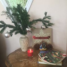 a small christmas tree sits on top of a table next to some books and a candle