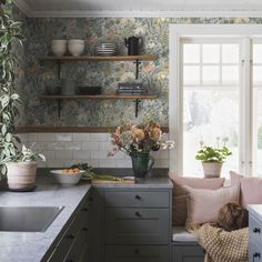 a dog is sitting on a bench in a kitchen with floral wallpaper and open shelving