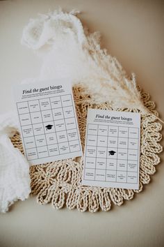 two pieces of paper on top of a doily next to some white yarn and a feather