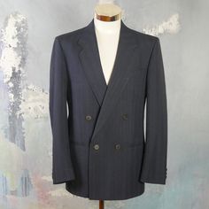 "This navy blue double-breasted blazer has notch lapels and padded shoulders, and closes in the front with one button (four in total show on the front). Three buttons decorate each sleeve cuff. The dark blue wool-blend jacket has three pockets on the front, and is fully lined in a navy blue satin viscose fabric (with two inner pockets). The fabric has a double pinstripe pattern, with a textured chevron herringbone running vertically as well. Brand label: Turo (Made in Finland) Size: 40 US/UK Mat Semi-formal Striped Sport Coat With Notch Lapel, Pinstripe Double-breasted Blazer With Notch Lapel, Pinstripe Notch Lapel Blazer With Double-breasted Button, Pinstripe Blazer With Notch Lapel And Double-breasted Buttons, Tailored Striped Suit With Double-breasted Fastening, Pinstripe Double-breasted Business Suit, Striped Double-breasted Suits For Business Casual, Classic Pinstripe Blazer With Double-breasted Button, Classic Pinstripe Double-breasted Blazer