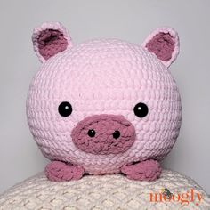 a pink crocheted pig sitting on top of a white pillow with black eyes