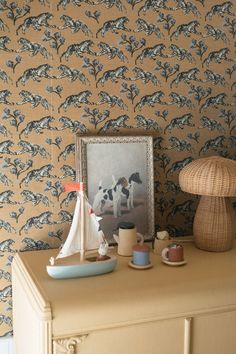 there is a small sailboat on the dresser next to a wallpapered room