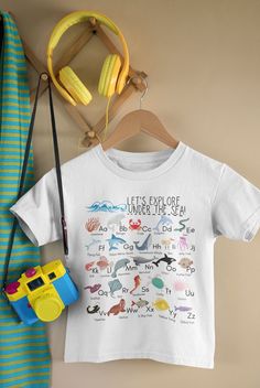 Delight your little ocean lover with this fun, one of a kind ocean animals alphabet shirt. Design features sea creatures from A-Z including many favorites- crab, dolphin, narwhal, orca, shark, and more! To Order, simply select your preferred color and size and add to your cart! Second shirt ships FREE! Check out our shop for lots of other one of a kind designs! I know you will love these fun prints as much as we do. To keep the designs on your new shirts looking great, wash inside out in cold wa Underwater Theme Class Shirts Juniors, Themed Multicolor T-shirt With Letter Print, White Character Print Tops For Beach, White Beach Tops With Character Print, White Tops For Ocean Activities In Summer, Themed Cotton T-shirt With Name Print, White Themed Letter Print Top, Cotton T-shirt For Summer Ocean Activities, Themed White Summer Tops