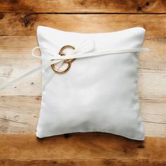 a white pillow with a gold ring tied to it on a wooden floor next to a pair of scissors