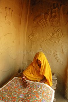 a woman sitting on top of a wooden bench in front of a wall with carvings