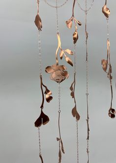 a metal wind chime with leaves and chains hanging from it's sides on a gray background