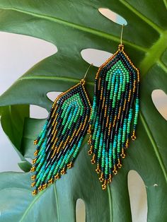 a pair of green and gold beaded earrings sitting on top of a large leaf