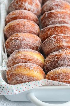 powdered sugar covered donuts in a white dish on a table with polka dot napkins