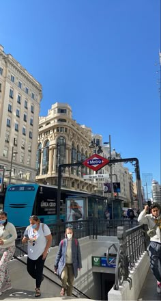 people are walking on the sidewalk in front of some buildings and traffic lights while wearing face masks