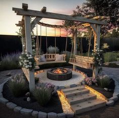 an outdoor fire pit with swings and seating around it at dusk or dawn, surrounded by flowers and greenery