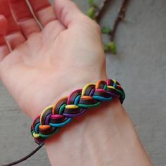 a hand holding a multicolored braid bracelet on it's left wrist,