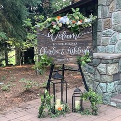 a welcome sign with candles and greenery on the side of a stone wall in front of a brick building