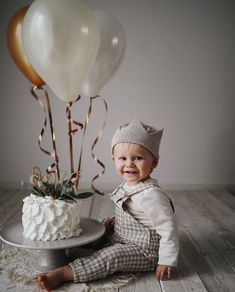 a baby sitting in front of a cake with balloons