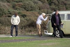 two men are standing next to an old vw bus and another man is holding the door open