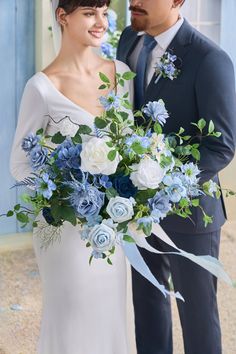 a bride and groom standing next to each other in front of a blue building with white flowers